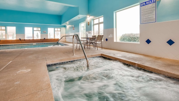 Une piscine intérieure avec un jacuzzi, des bancs et un panneau indiquant les « RÈGLES DU SPA ».