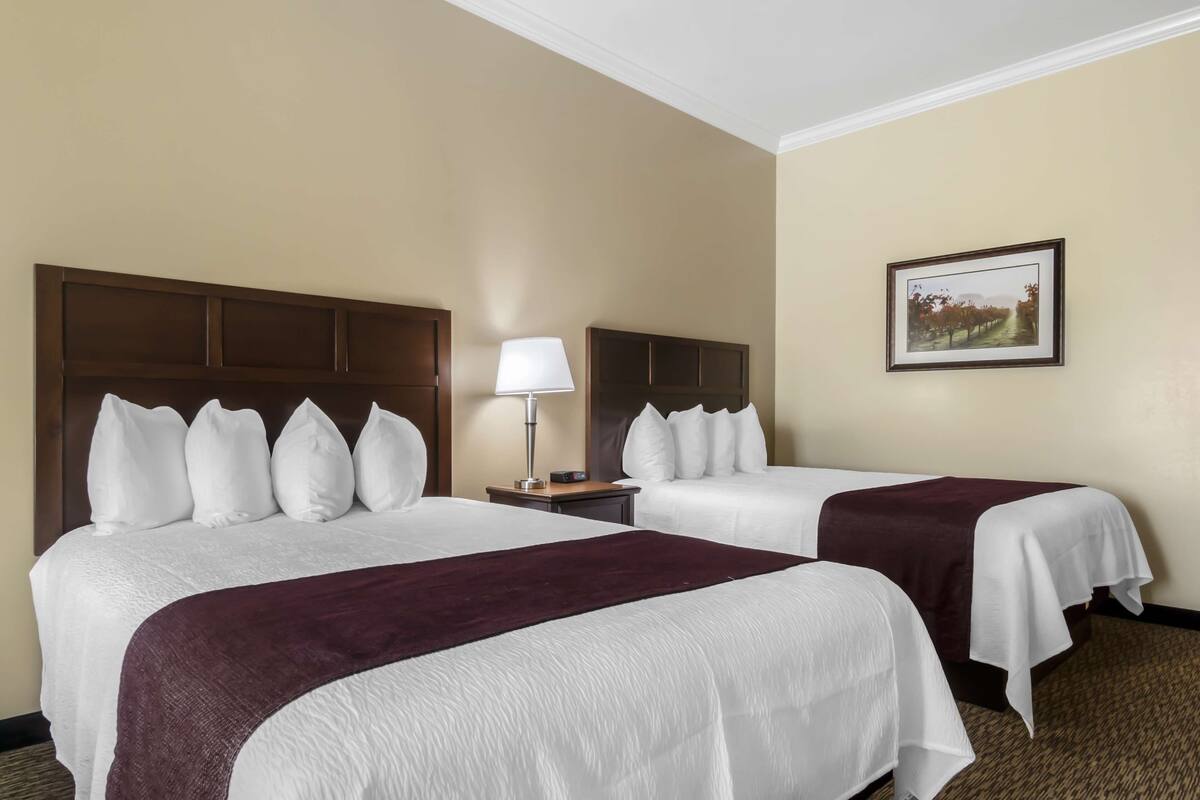 A hotel room with two beds, a nightstand with a lamp, and a framed picture on the wall.