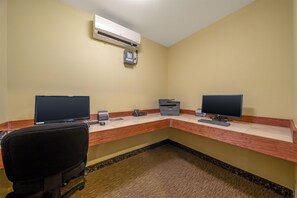 A hotel office with two computer desks, a chair, an air conditioner, and a printer.