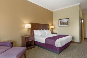 A hotel room with a bed, two bedside lamps, a nightstand, a chair, a framed picture on the wall, and a door.