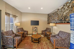 A hotel lobby with a flat-screen TV mounted on the wall, patterned sofas, a coffee table, and a bulletin board with various items pinned to it. - Best Western Plus Grapevine Inn (Sunnyside)