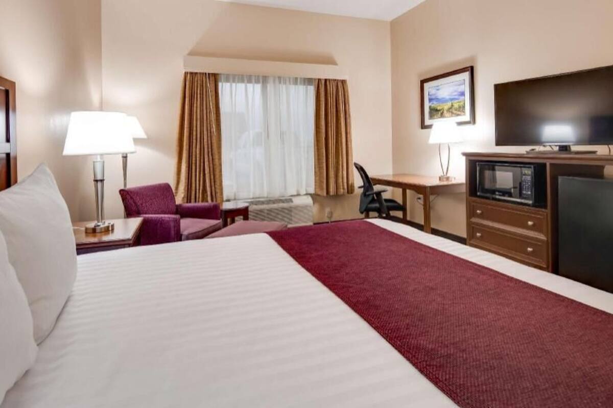 A hotel room with a large bed, a desk with a chair, a television, a microwave, and a small refrigerator.