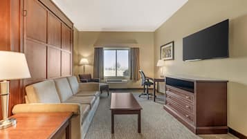 A hotel room with a sofa, a desk, a chair, a dresser, a flat-screen TV, and a window with a view.