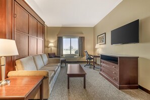 A hotel room with a sofa, a desk, a chair, a dresser, a flat-screen TV, and a window with a view. - Best Western Plus Grapevine Inn (Sunnyside)