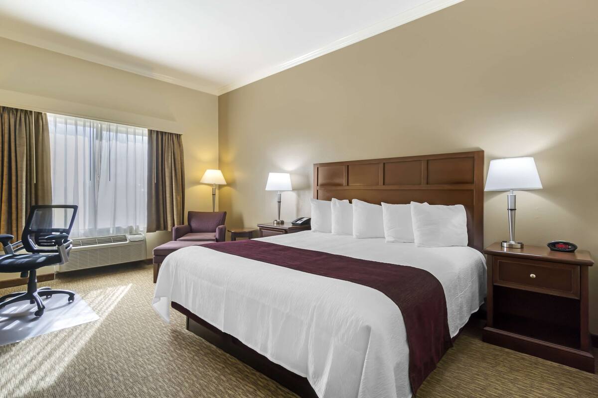 A hotel room with a large bed, two bedside tables with lamps, a chair, a desk, and a window with curtains.