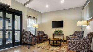 Un hall d’hôtel doté d’un espace salon comprenant des fauteuils à motifs, une table basse ronde et un téléviseur à écran plat fixé au mur.