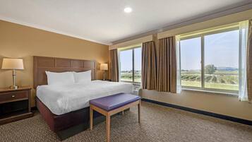 A hotel room with a large bed, two bedside lamps, a bench, and a window with curtains.