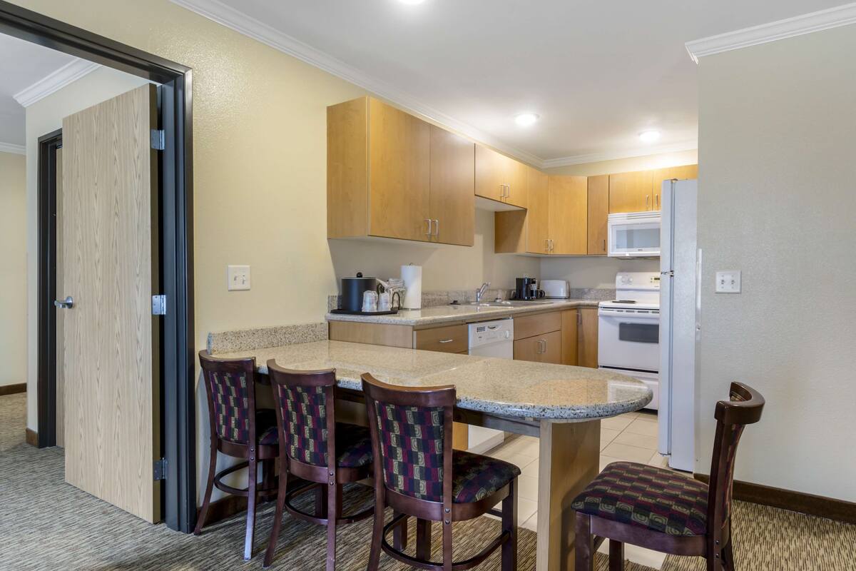 A compact kitchen with wooden cabinets, a microwave, a refrigerator, and a dining area with two chairs and a table.
