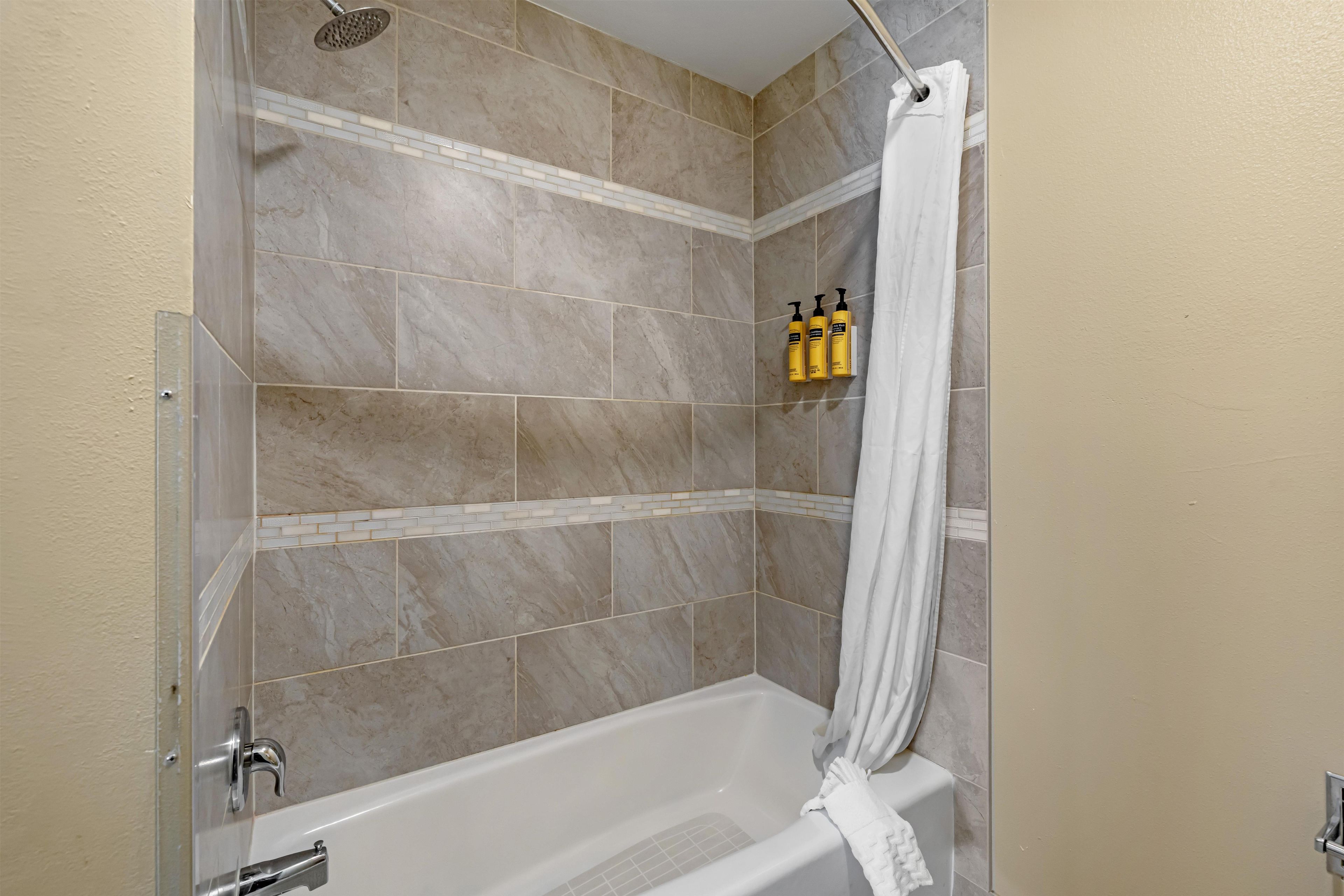 A bathroom with a shower, a bathtub, and a towel rack with bottles.