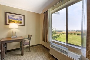 Ein Hotelzimmer mit Schreibtisch, Stuhl, Lampe und einem großen Fenster mit Blick auf einen Weinberg.