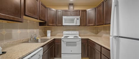 A kitchen with dark wooden cabinets, white appliances, and a speckled tile backsplash.