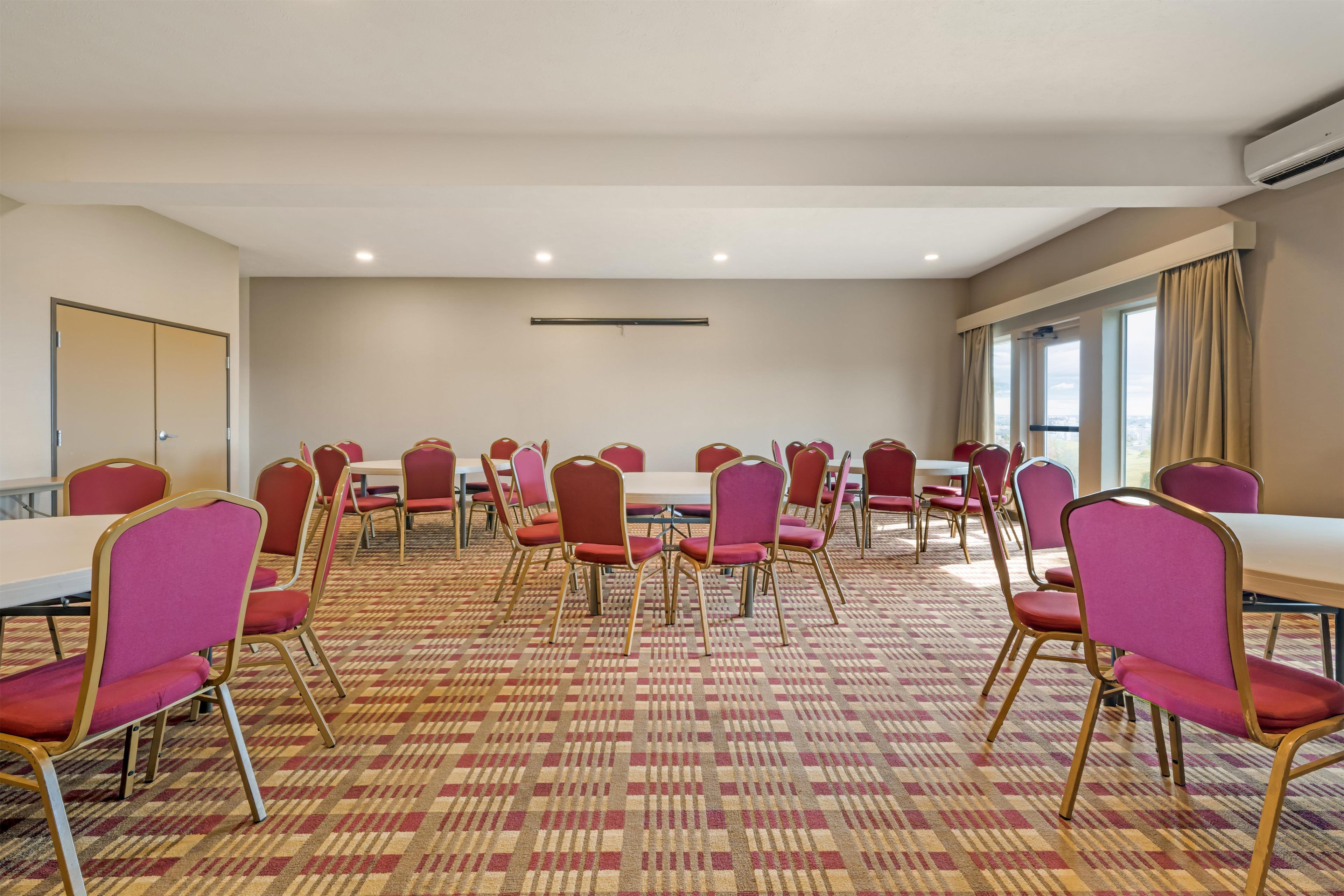 A conference room with round tables and chairs, a patterned carpet, and a large window with curtains.