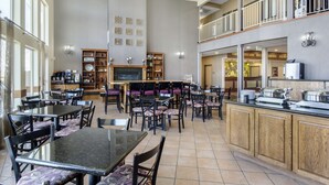 Un vaste espace dédié à la salle à manger, avec de nombreuses tables et chaises, une cheminée centrale et un buffet.