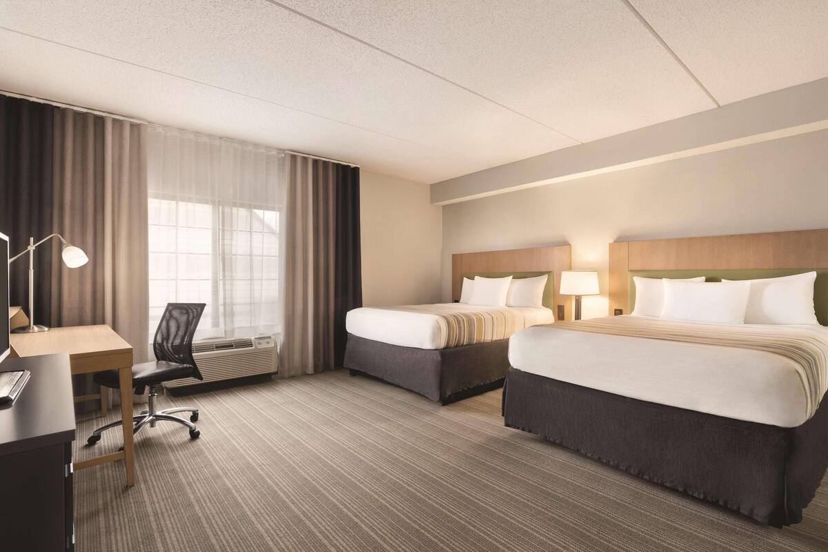 A hotel room with two beds, a desk, a chair, and a large window with curtains.