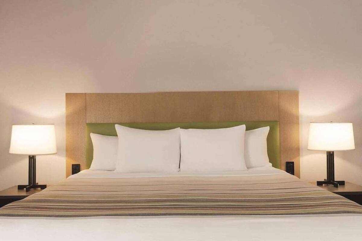 A hotel room with a bed, two bedside lamps, and a headboard.