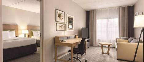 A hotel room with a bed, desk, chair, TV, sofa, and a small table.