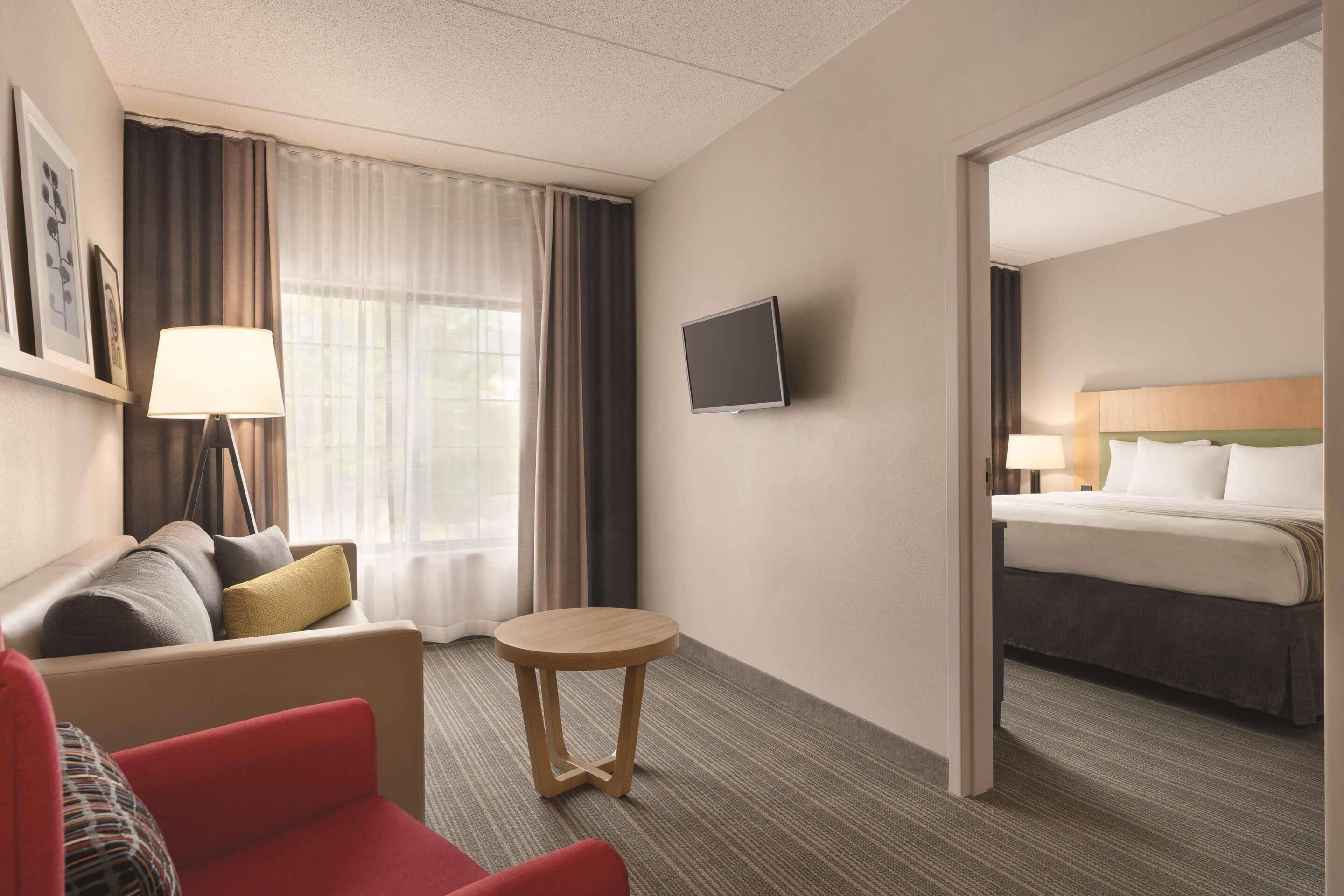 A hotel room with a sofa, a small round table, a bed, and a TV mounted on the wall.