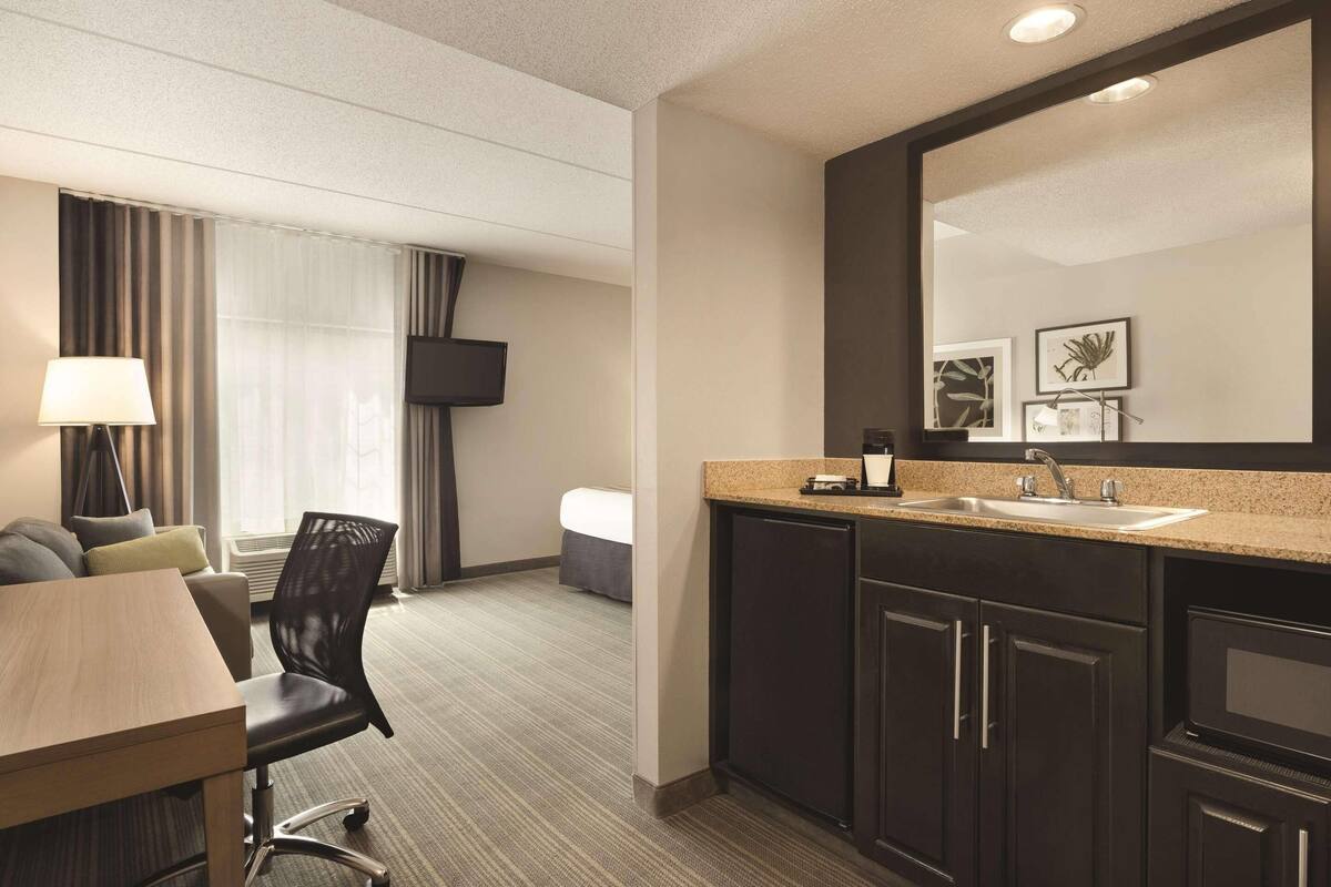 A modern hotel room with a dining area, a large mirror, a sink, and a flat-screen TV.