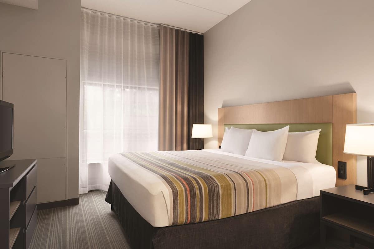 A hotel room with a bed, a TV, a desk, a lamp, and a window with curtains.