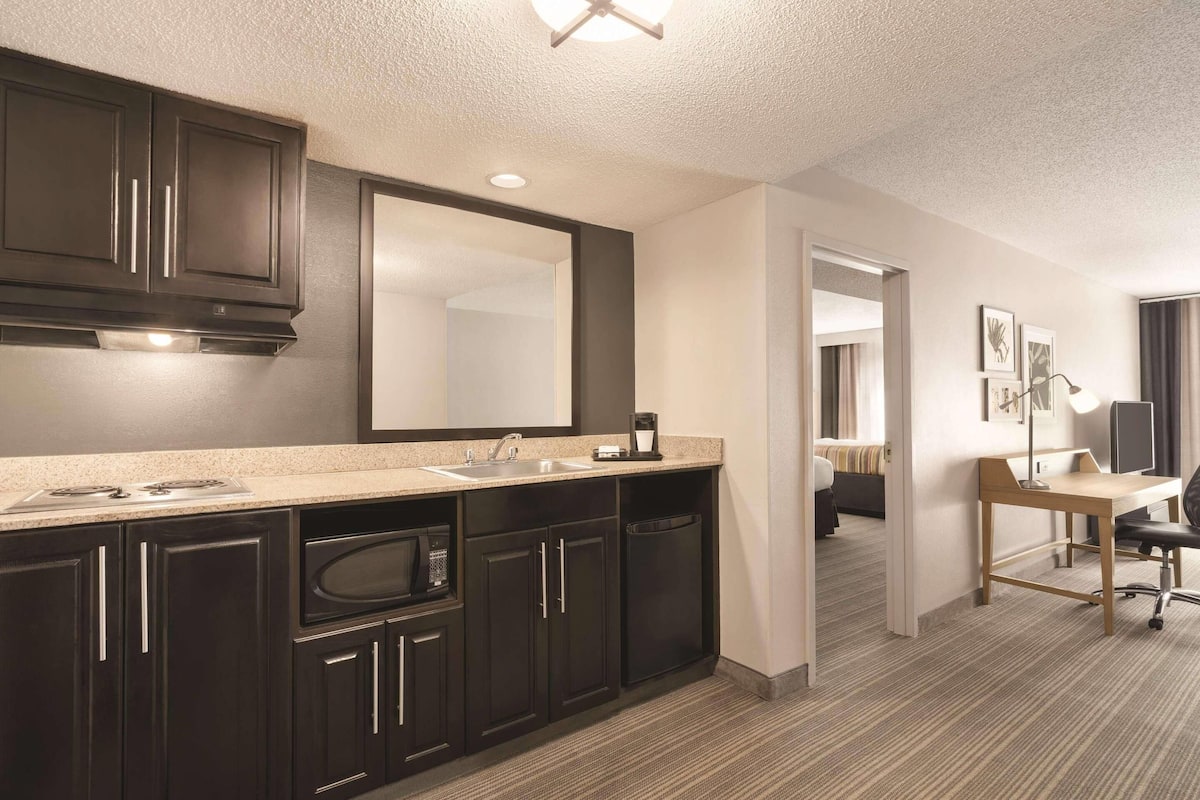 A modern hotel bathroom with dark cabinetry, a large mirror, a sink, and a countertop with a coffee maker.