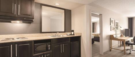 A modern hotel bathroom with dark cabinetry, a large mirror, a sink, and a countertop with a coffee maker.