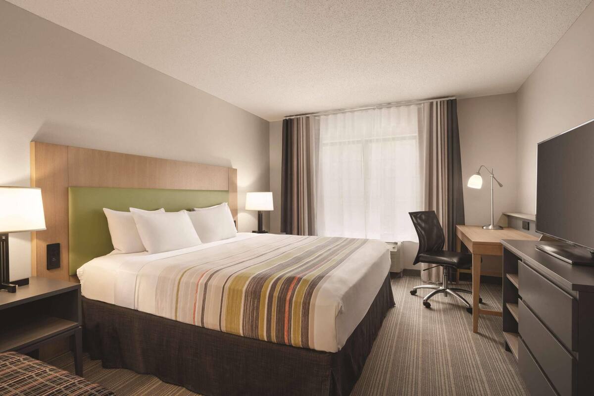 A hotel room with a large bed, a desk, a chair, a TV, and a window with curtains.