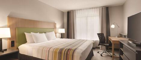 A hotel room with a large bed, a desk, a chair, a TV, and a window with curtains.