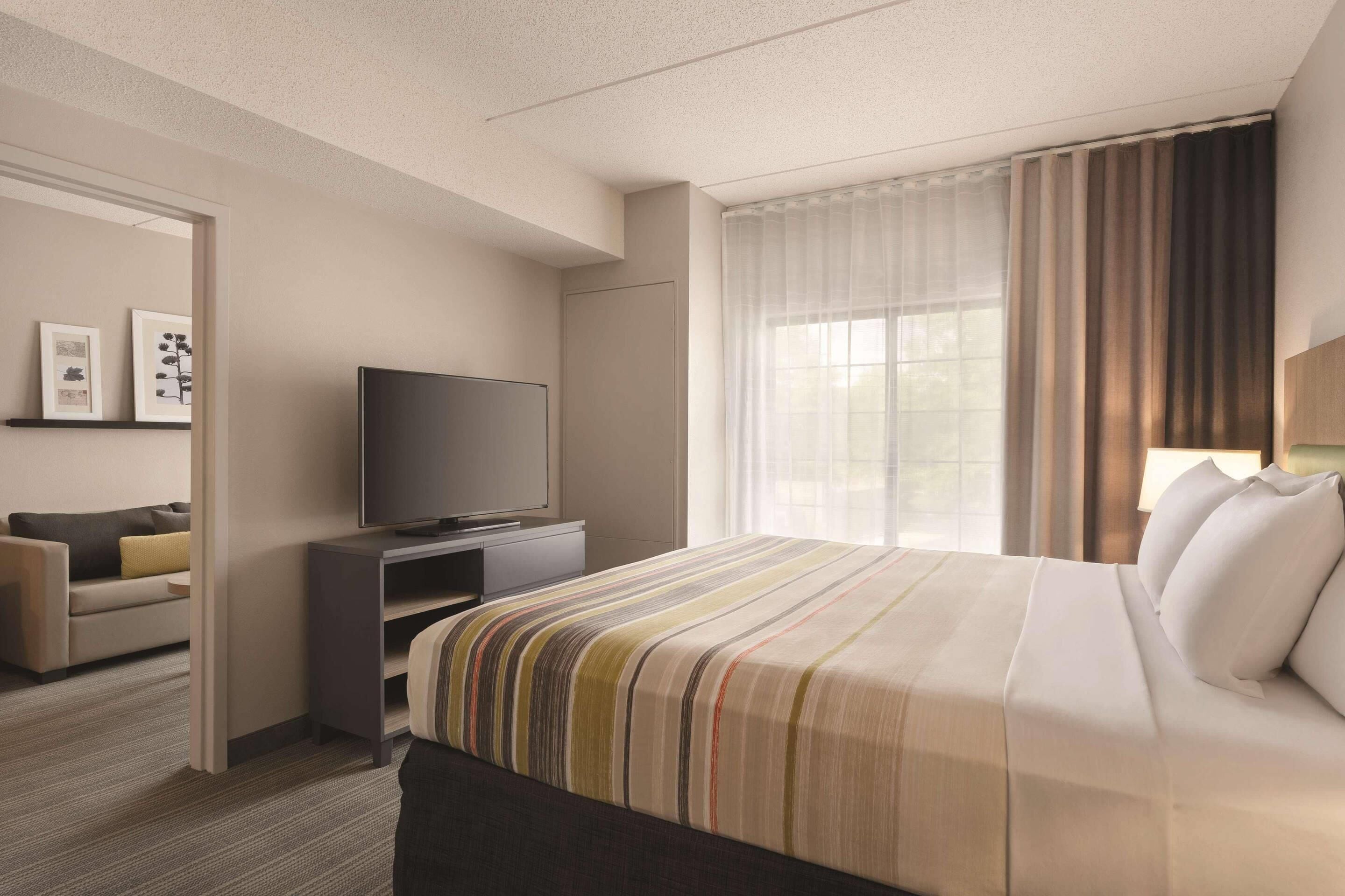 A hotel room with a bed, a TV, a sofa, and a window with curtains.