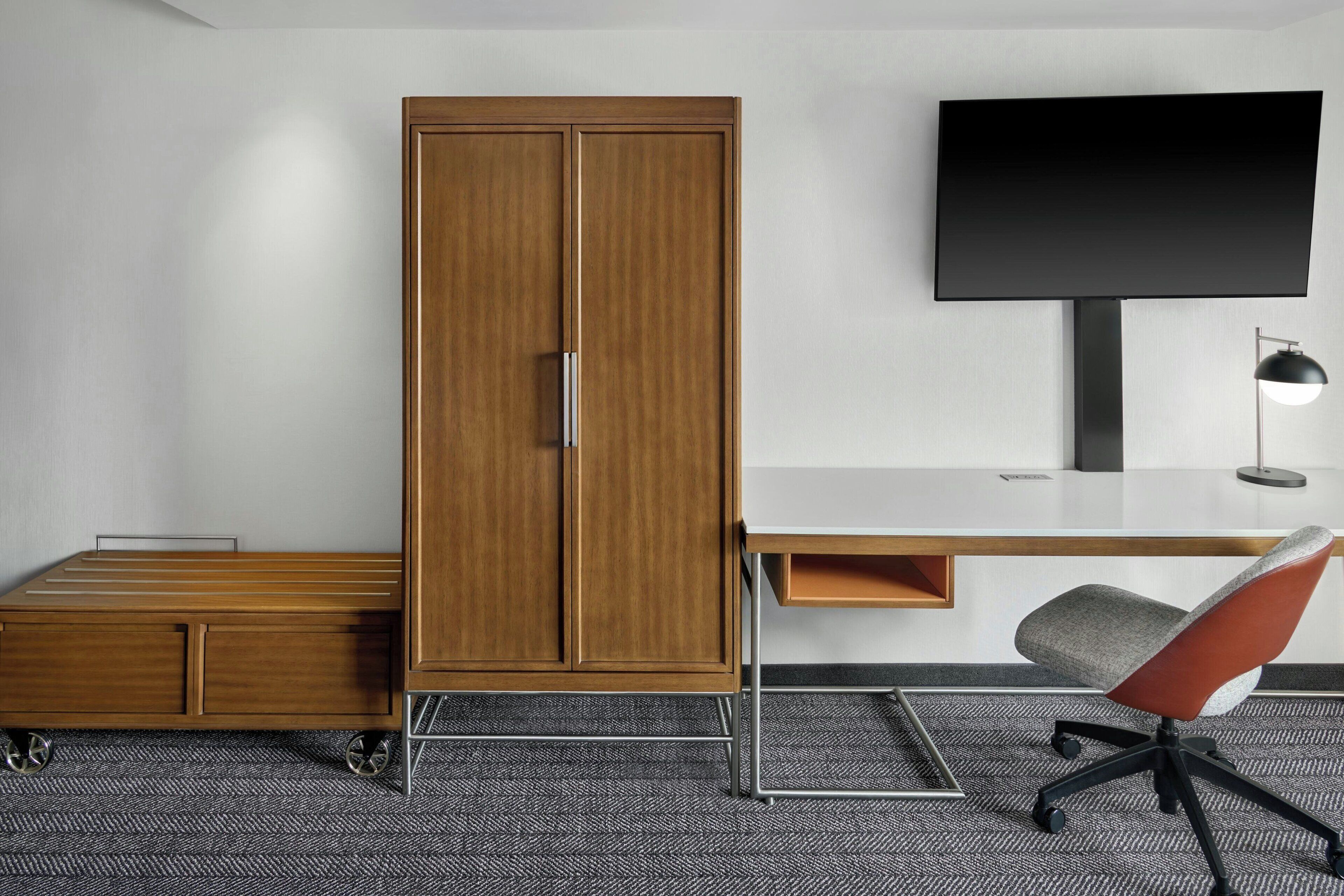 Une chambre d’hôtel moderne équipée d’une armoire en bois, d’un téléviseur à écran plat, d’un bureau avec une chaise et d’une lampe de bureau.