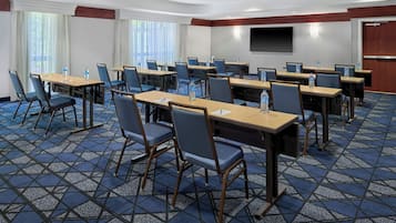 Une salle de conférence dotée de plusieurs tables et chaises, équipée de bouteilles d’eau, située dans un hôtel.