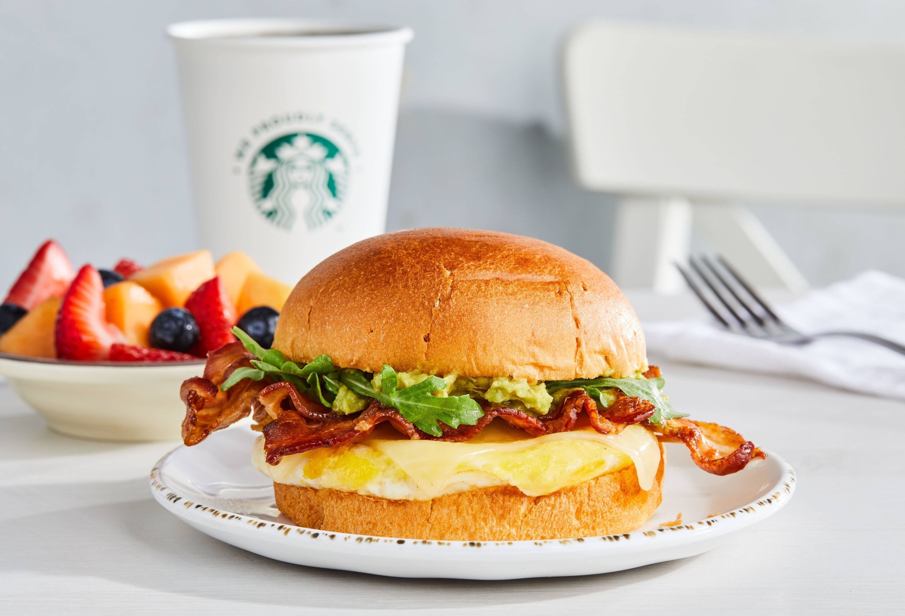 Un sándwich de desayuno sobre un plato con una taza de Starbucks al fondo.