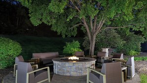 Un patio al aire libre con fogón de piedra y asientos, además de un árbol.