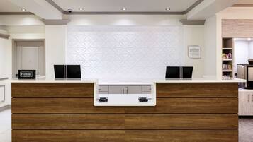 Ein modern gestalteter Hotelrezeptionstresen mit weiß-holzfarbenem Design, einer Wand mit geometrischem Muster und einem Schild mit der Aufschrift 'Hilton Honors'.
