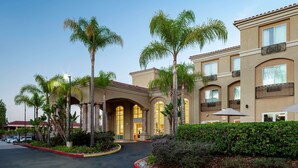 A hotel with a central courtyard, palm trees, and a red curb. - Hilton Garden Inn San Diego - Rancho Bernardo (San Diego)