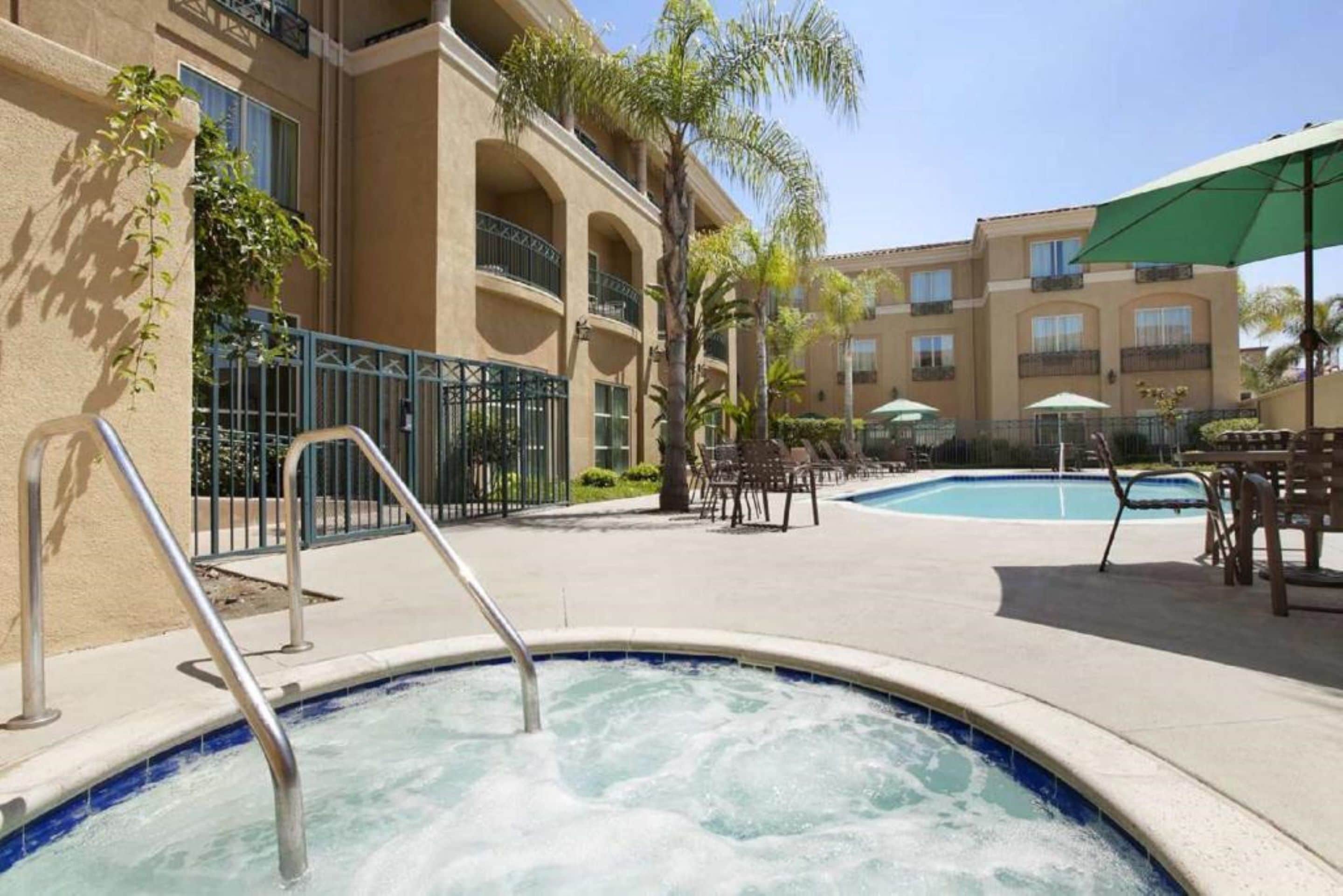 A hotel pool area with a hot tub, outdoor seating, and a building with balconies.