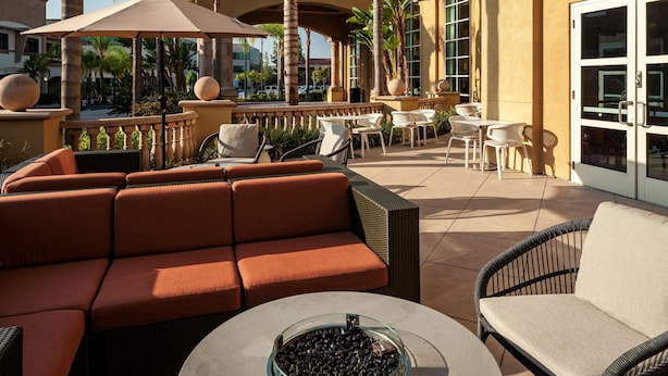 An outdoor patio with seating, umbrellas, and palm trees. - Hilton Garden Inn San Diego - Rancho Bernardo (San Diego)
