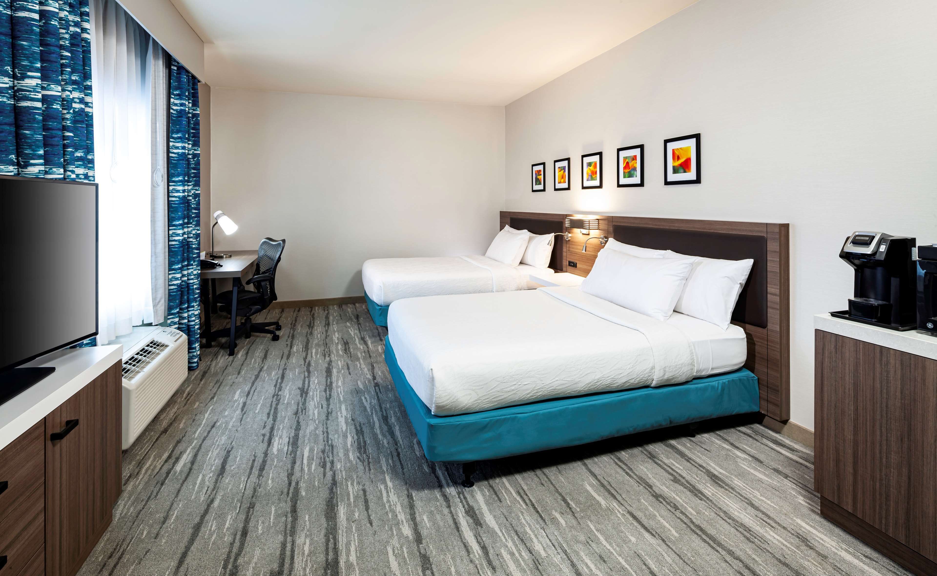 A hotel room with two beds, a desk with a chair, a TV, and a coffee machine.