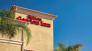 Exterior de un Hilton Garden Inn con un cielo azul despejado al fondo.