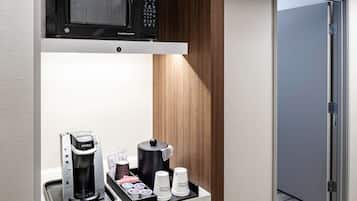 A hotel room with a microwave on a shelf, a coffee maker, and a coffee station with cups and creamer.