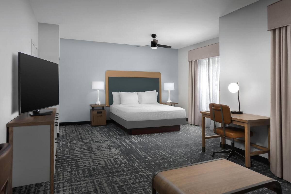 Une chambre d’hôtel équipée d’un lit, d’un bureau, d’une chaise, d’une télévision et d’un ventilateur de plafond.