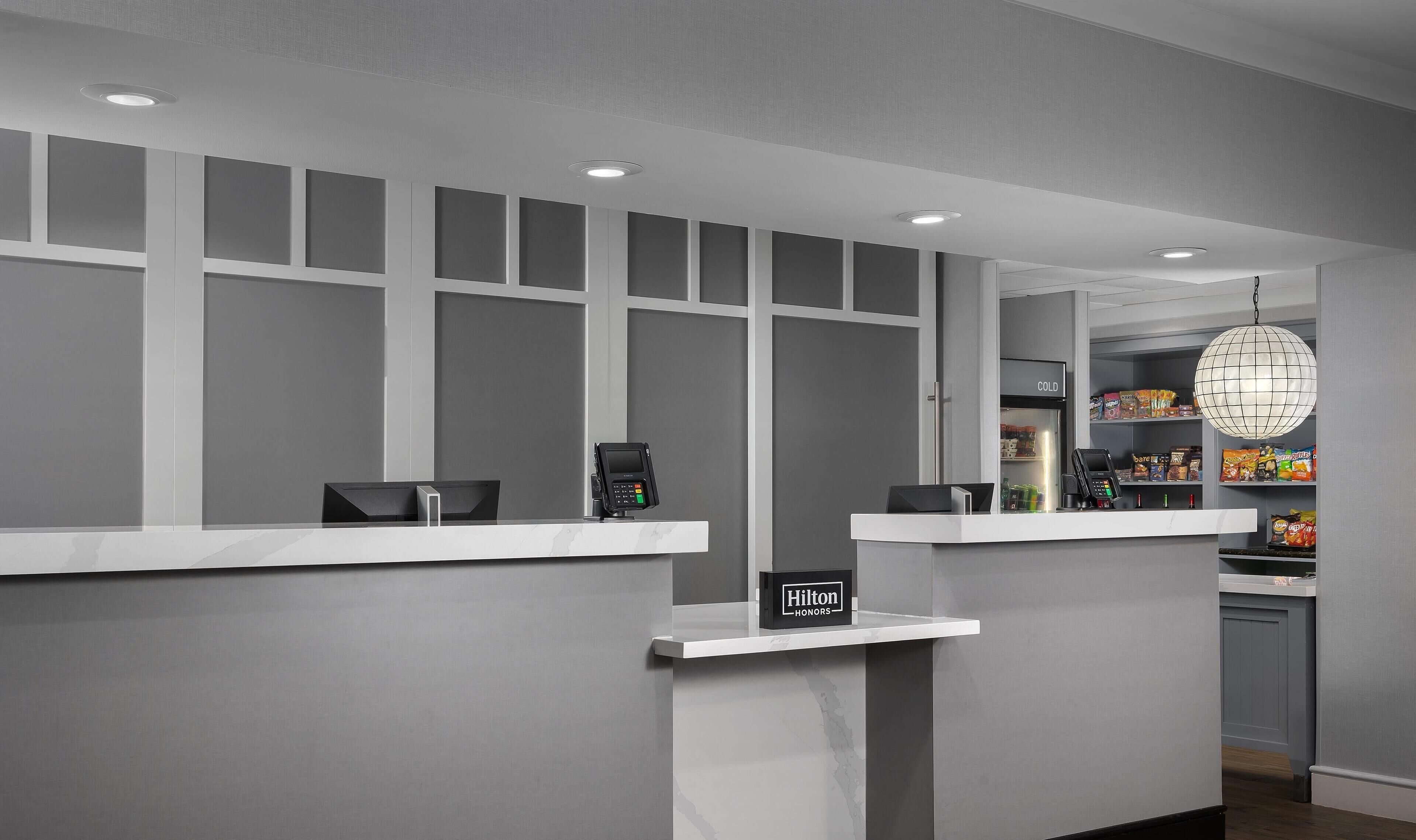 Een receptie van een hotel met een modern design, met een balie, een betaalterminal, een minibar en een bord met de naam van het merk.