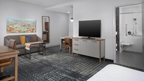 Une chambre d’hôtel moderne équipée d’un canapé, d’un bureau avec un téléviseur à écran plat, d’un lit et d’un espace douche.