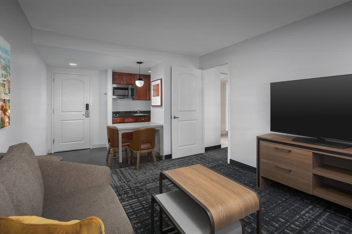 Une chambre d’hôtel moderne équipée d’un canapé, d’une table à manger, d’un téléviseur et d’un coin cuisine.