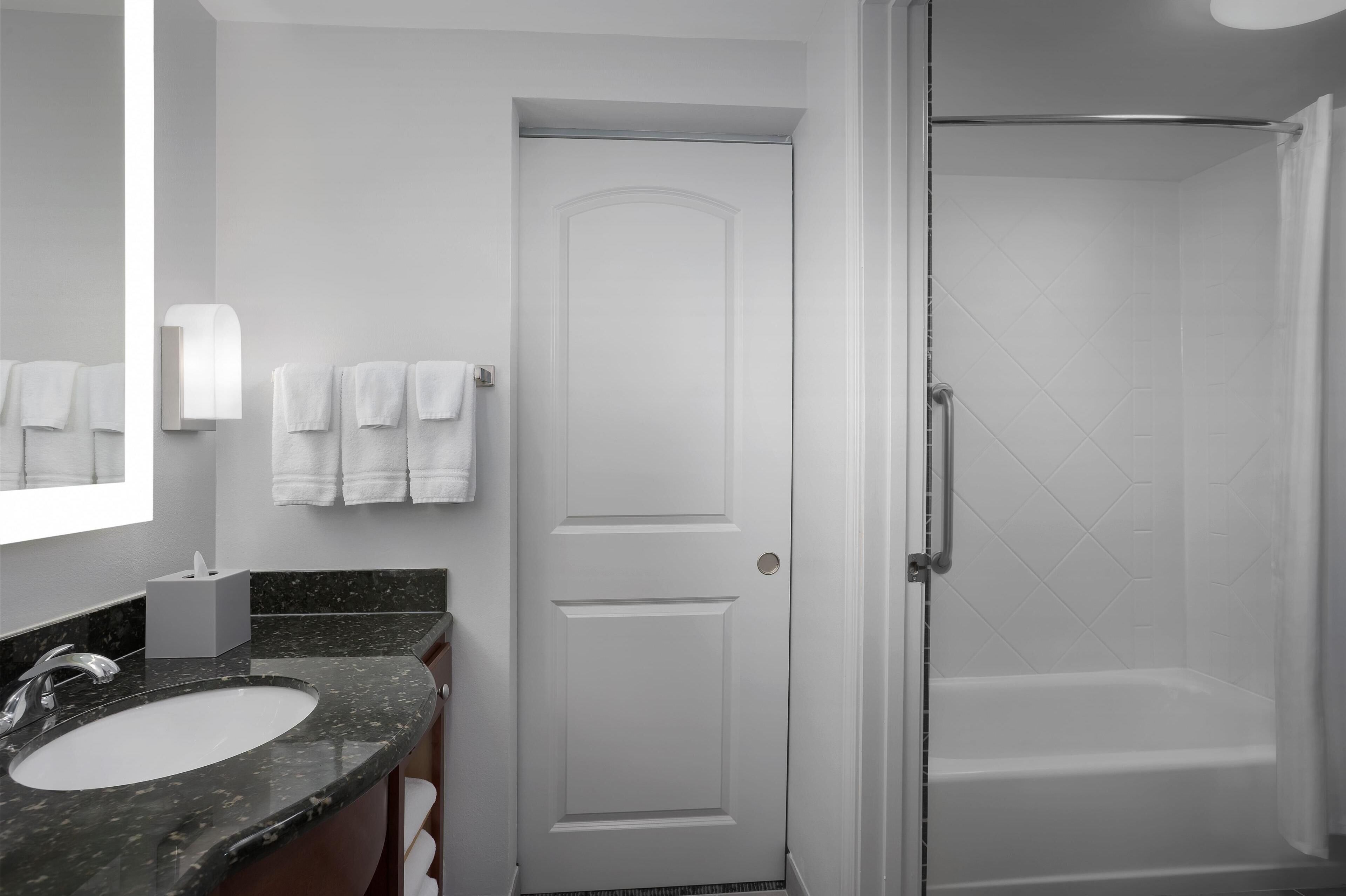 A bathroom with a white door, a sink with a marble countertop, and a shower area.