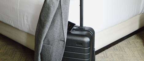 Una habitación de hotel con una cama, una lámpara, una maleta y una chaqueta encima de la maleta.