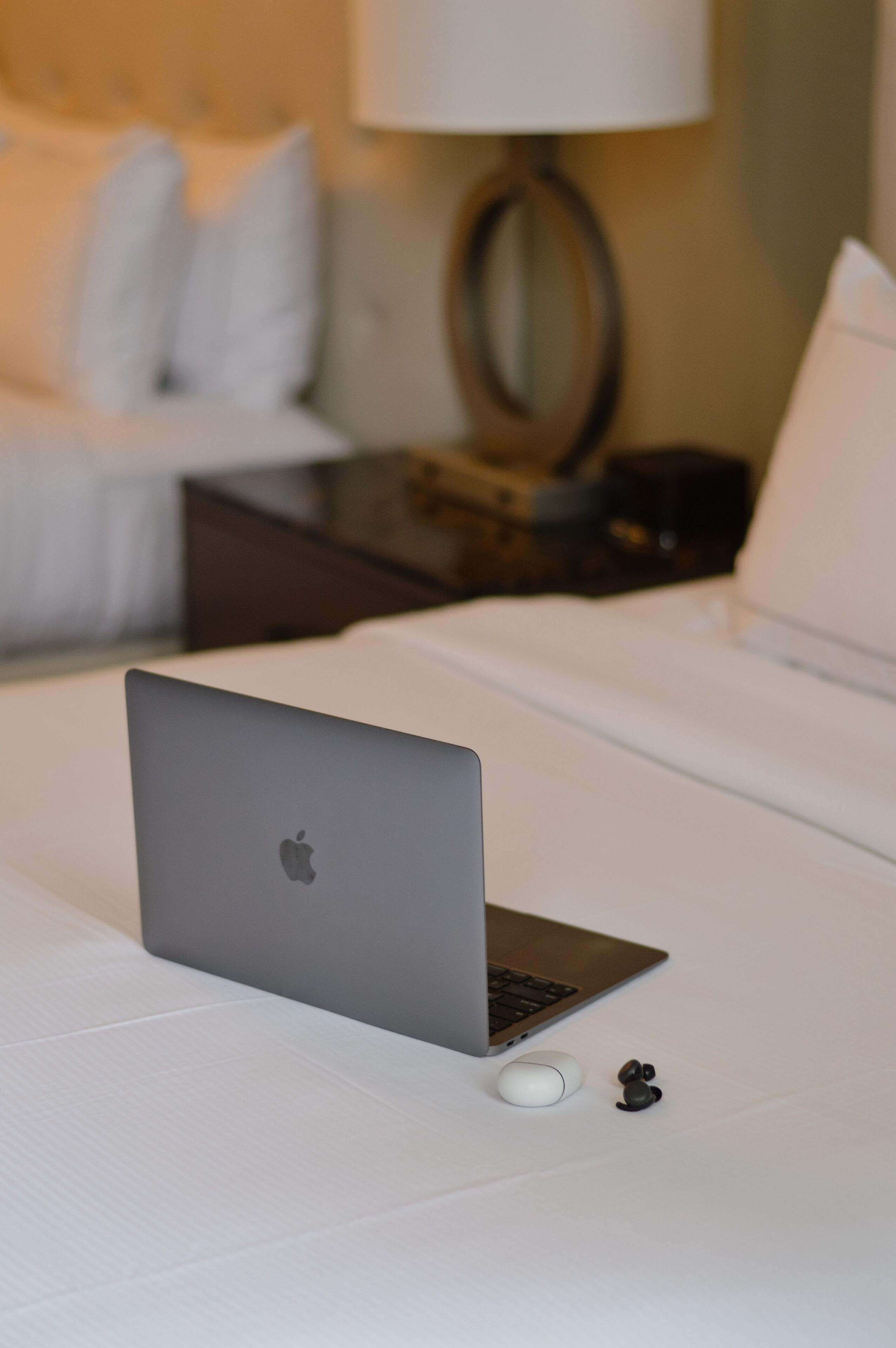 A laptop on a bed with a white mouse and earbuds beside it.