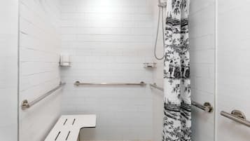 A bathroom with white tiled walls, a shower with a black and white patterned curtain, a grab bar, and a white bench.