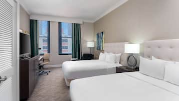 A hotel room with two beds, a desk, a chair, a TV, and a window with curtains.