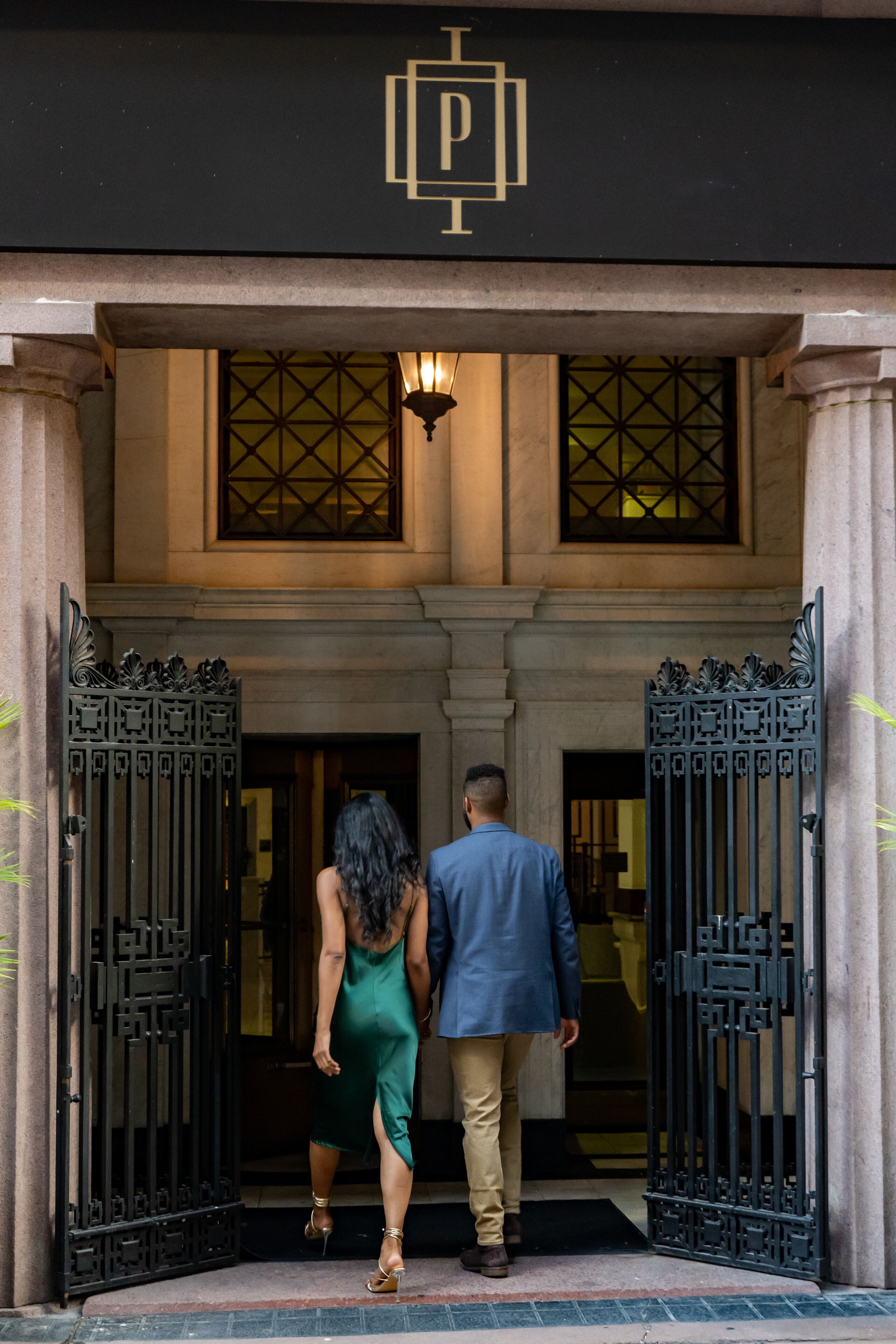 A man and a woman exiting a building through a black wrought iron gate.