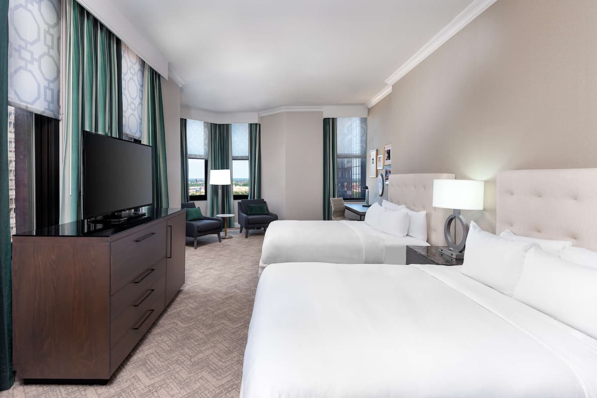 A hotel room with two beds, a TV, a desk, and a chair.